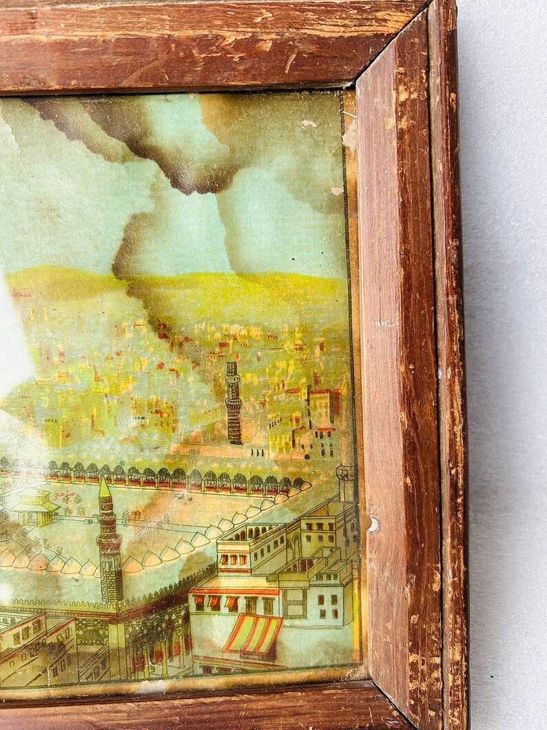 Puede incluir: Una ilustraci&oacute;n vintage enmarcada de una ciudad con una mezquita en primer plano. La ilustraci&oacute;n est&aacute; pintada en colores apagados con un cielo azul y edificios amarillos. El marco es de madera y tiene un acabado desgastado.