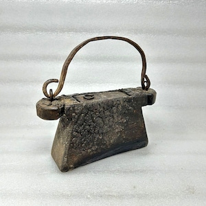May include: A dark brown, weathered wooden object with a curved metal handle. The wood has a textured, aged appearance. The handle is attached to the top of the rectangular block. The object appears to be an antique or vintage item.