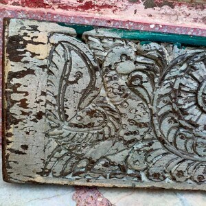 May include: A weathered wooden panel with intricate carvings of a bird and floral designs. The wood is painted white and shows signs of age and wear.