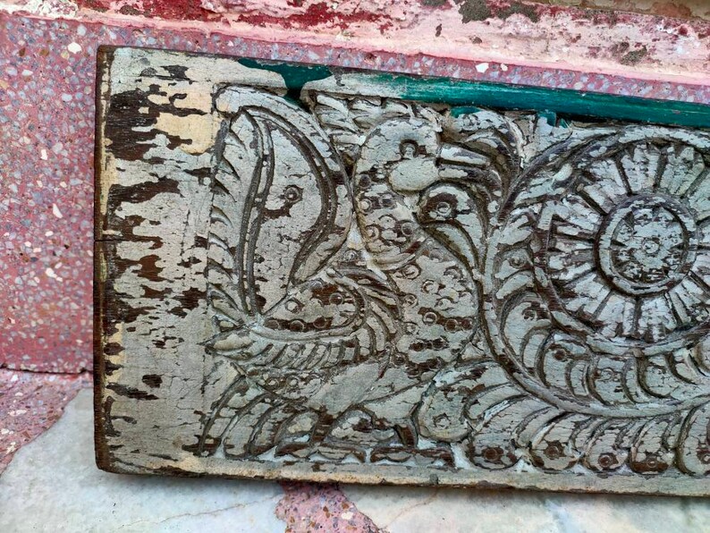 May include: A weathered wooden panel with intricate carvings of a bird and floral designs. The wood is painted white and shows signs of age and wear.