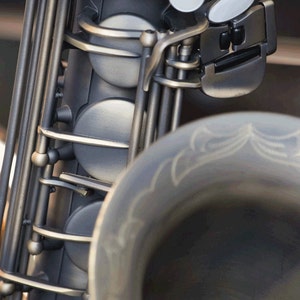 May include: Close-up of a silver saxophone with a black key mechanism and white pads. The saxophone is in focus, while the background is blurred.