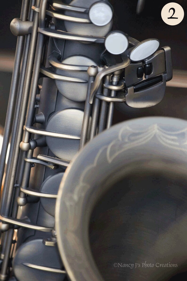 May include: Close-up of a silver saxophone with a black key mechanism and white pads. The saxophone is in focus, while the background is blurred.