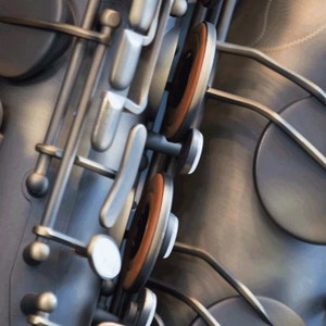 May include: Close-up of a silver saxophone with brown key pads. The saxophone is made of metal and has a shiny finish.