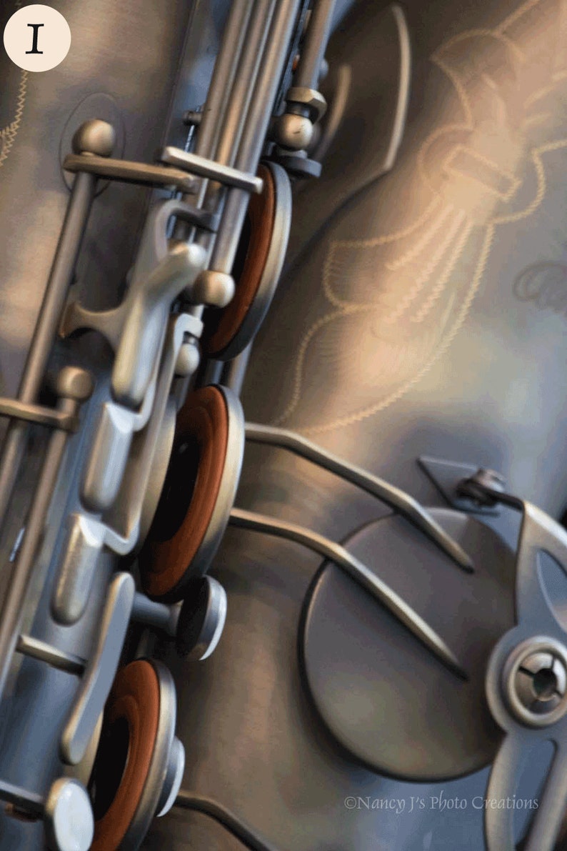 May include: Close-up of a silver saxophone with brown leather pads. The saxophone has a decorative design on the body.