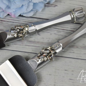May include: Silver cake knife and server set with rhinestone embellishments. The handles are silver and the blades are black.