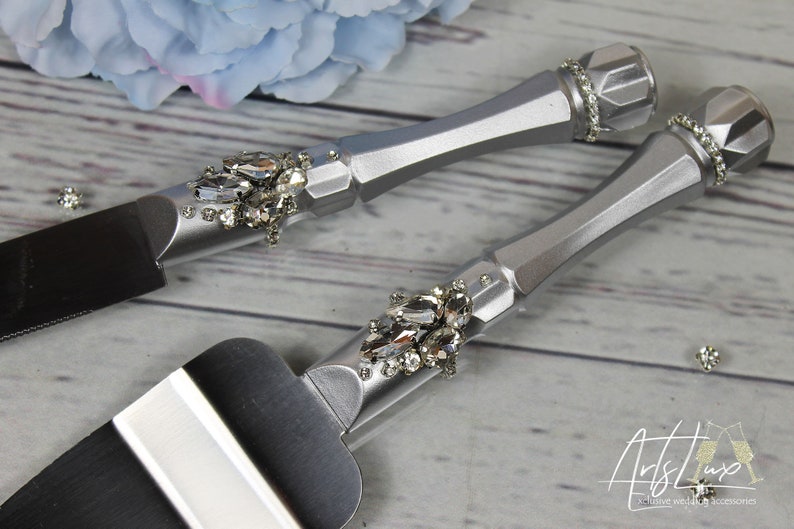 May include: Silver cake knife and server set with rhinestone embellishments. The handles are silver and the blades are black.