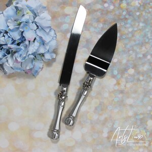 May include: A silver cake knife and server set with ornate handles featuring rhinestones. The handles are silver and the blades are stainless steel.