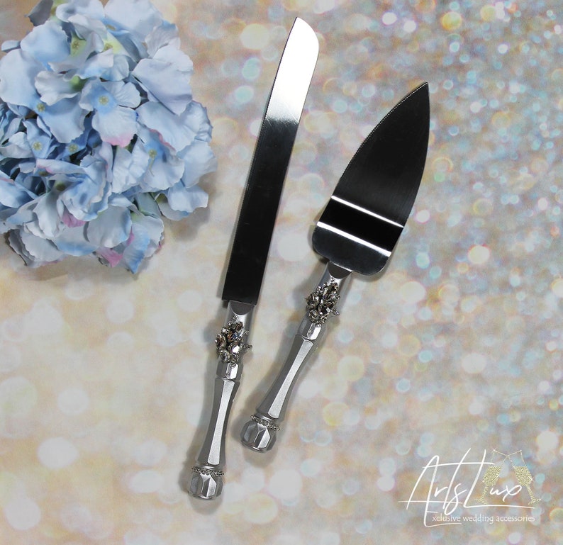 May include: A silver cake knife and server set with ornate handles featuring rhinestones. The handles are silver and the blades are stainless steel.