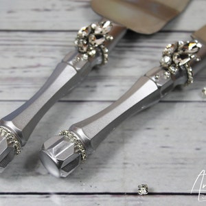 May include: A set of silver wedding cake cutting knives with rhinestone embellishments. The knives have a silver finish and are decorated with sparkling rhinestones.