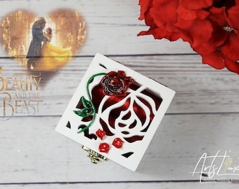 May include: White wooden box with a red rose design. The box has a red velvet interior and a gold latch. The box is decorated with a red rose and green leaves. The box is a ring box.