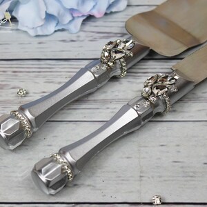 May include: A silver cake knife and server set with rhinestone embellishments. The handles are silver and the blades are stainless steel.
