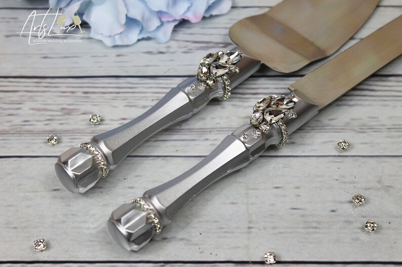 May include: A silver cake knife and server set with rhinestone embellishments. The handles are silver and the blades are stainless steel.