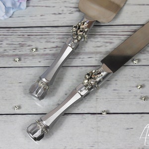 May include: A silver cake knife and server set with rhinestone embellishments. The handles are silver and the blades are stainless steel.