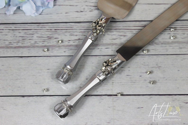 May include: A silver cake knife and server set with rhinestone embellishments. The handles are silver and the blades are stainless steel.