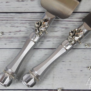May include: Silver cake knife and server set with rhinestone embellishments. The handles are silver and have a geometric design. The blades are stainless steel.