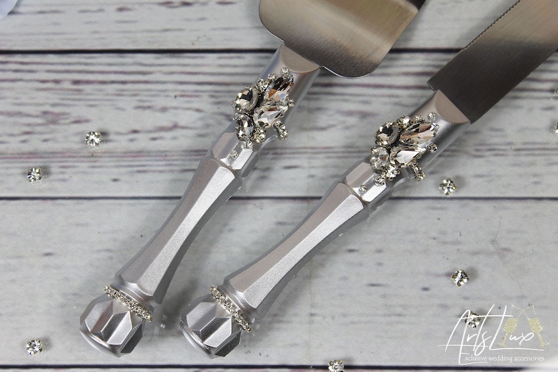 May include: Silver cake knife and server set with rhinestone embellishments. The handles are silver and have a geometric design. The blades are stainless steel.