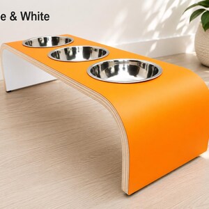 Modern orange and white raised triple dog bowl stand with stainless steel bowls, handcrafted curved wooden pet feeder for dogs and cats.