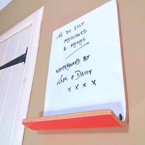 Angled view of dry erase whiteboard with shelf for storage. Various colours available for the rear of board. Has natural wood trim and is wall mounted.