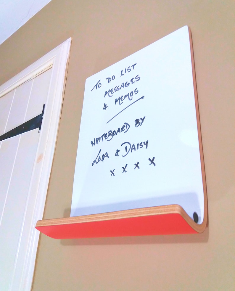 Angled view of dry erase whiteboard with shelf for storage. Various colours available for the rear of board. Has natural wood trim and is wall mounted.