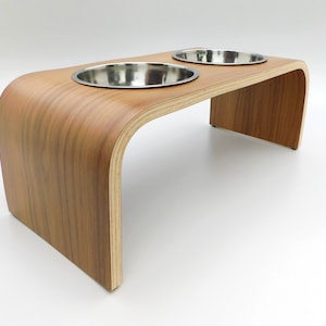 Angled view of a wooden dog bowl stand in a walnut finish holding 2 stainless steel bowls and a natural wood trim on a white background.