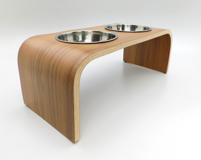 Angled view of a wooden dog bowl stand in a walnut finish holding 2 stainless steel bowls and a natural wood trim on a white background.