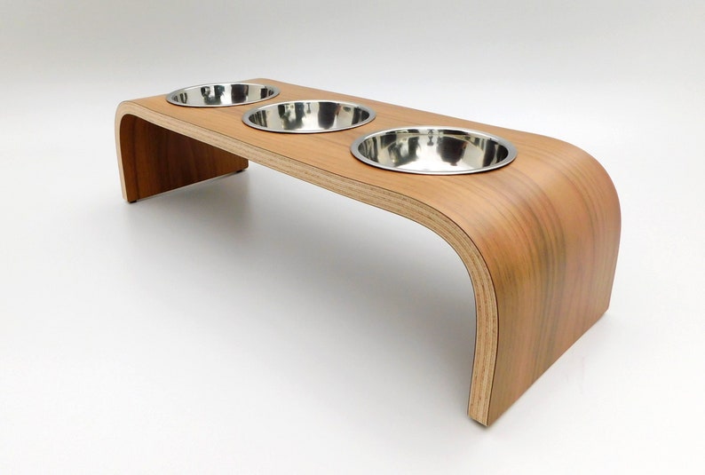 Angled view of our triple bowl raised dog feeder in a walnut finish on a white background with three stainless steel bowls and showing the natural wood edge finish.