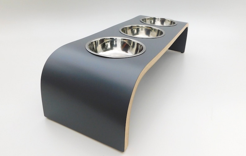 Angled view of our triple bowl raised dog feeder in a dark grey finish on a white background with three stainless steel bowls and showing the natural wood edge finish.