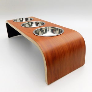 Angled view of our triple bowl raised dog feeder in a cherry wood and black finish on a white background with three stainless steel bowls and showing the natural wood edge finish.