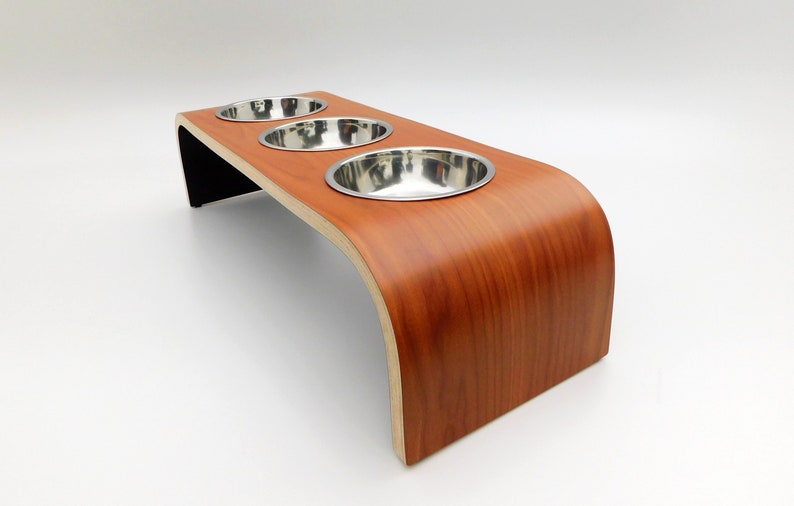 Angled view of our triple bowl raised dog feeder in a cherry wood and black finish on a white background with three stainless steel bowls and showing the natural wood edge finish.