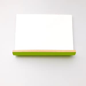 Front view of a whiteboard with green on the reverse in landscape form with a shelf ideal for pens or keys with a natural wood trim on a wall.