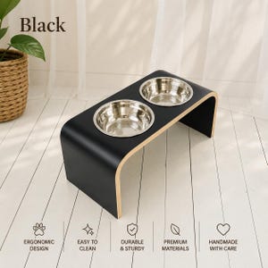 Black raised wooden dog bowl stand with stainless steel bowls, handmade elevated pet feeder in a modern interior, stylish feeding station for dogs and cats.