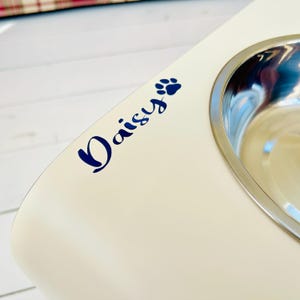 cream coloured wooden dog feeding station personalised with the dog name 'Daisy' in blue vinyl lettering