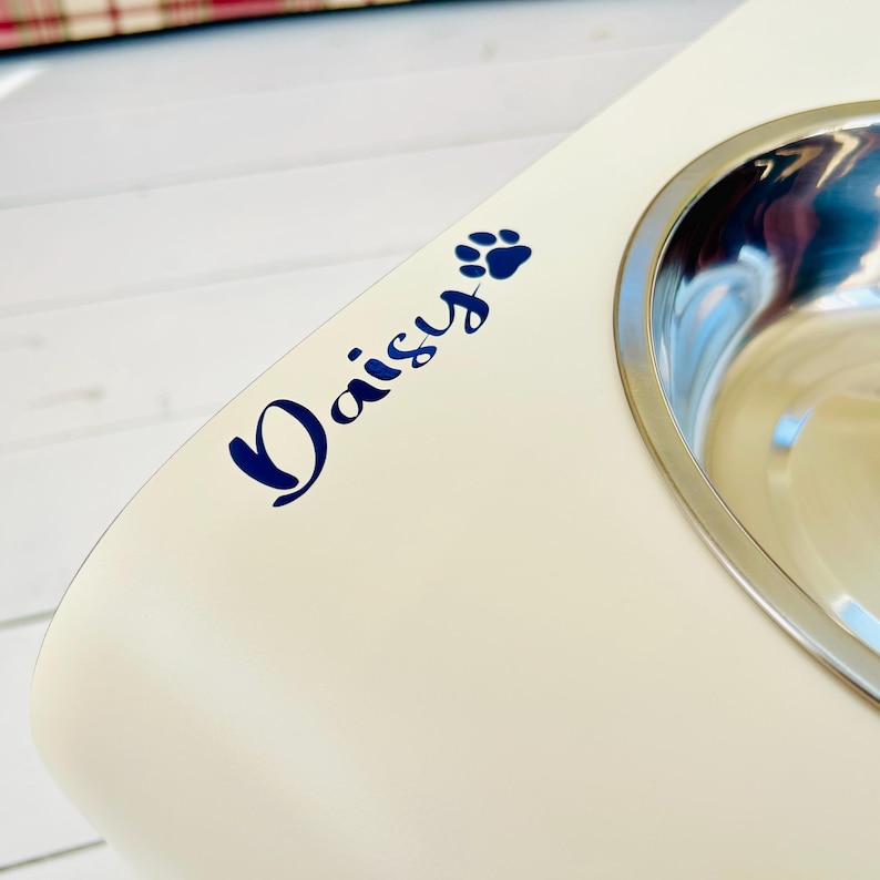 cream coloured wooden dog feeding station personalised with the dog name 'Daisy' in blue vinyl lettering