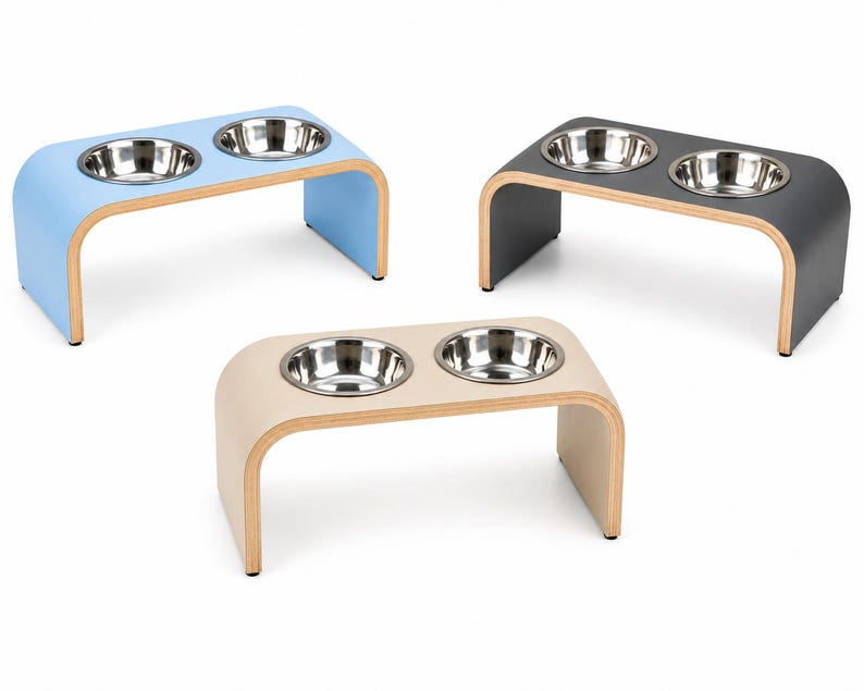 Three handmade double raised pet feeders in Hemp (Beige), Powder Blue, and Graphite Grey finishes, each featuring a modern curved wooden design with two removable stainless steel bowls. Premium elevated feeding stations for cats and dogs with durable, easy-clean laminate surfaces, displayed on a clean white background for easy colour comparison.