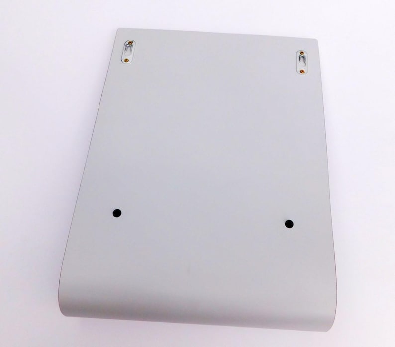 May include: A white, rectangular wall shelf with rounded edges and two small black dots on the front. The shelf has two small, silver-colored hooks on the top, one on each side.