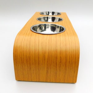 End view of our triple bowl raised dog feeder in a light oak finish on a white background with three stainless steel bowls and showing the natural wood edge finish.