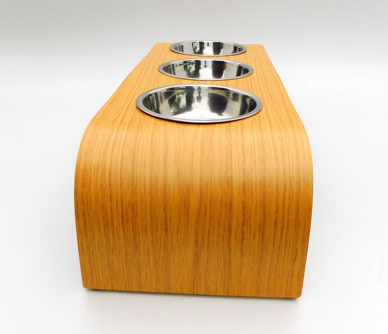 End view of our triple bowl raised dog feeder in a light oak finish on a white background with three stainless steel bowls and showing the natural wood edge finish.