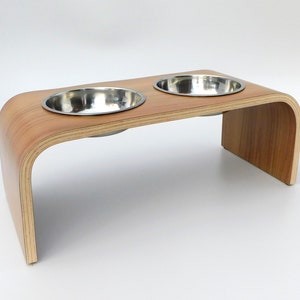 Angled view of raised pet feeder made from Formica easy to clean in a walnut finish holding 2 stainless steel bowls and a natural wood trim on a white background.