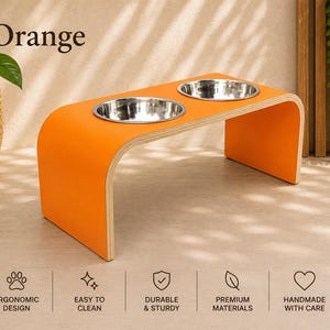 Orange elevated dog bowl stand with stainless steel bowls, handmade wooden pet feeder in a contemporary home, modern feeding station for dogs and cats.