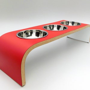 Angled view of our triple bowl raised dog feeder in a red and white finish on a white background with three stainless steel bowls and showing the natural wood edge finish.