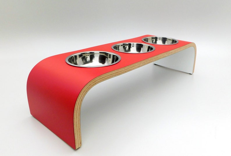 Angled view of our triple bowl raised dog feeder in a red and white finish on a white background with three stainless steel bowls and showing the natural wood edge finish.