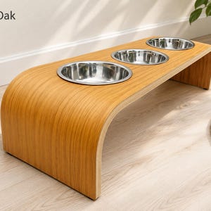 Modern light oak raised triple dog bowl stand with stainless steel bowls, handcrafted curved wooden pet feeder for dogs and cats.