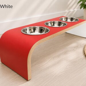 Modern red and white raised triple dog bowl stand with stainless steel bowls, handcrafted curved wooden pet feeder for dogs and cats.