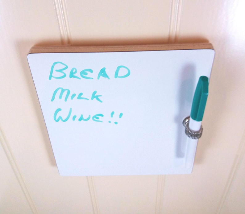 Top view of small whiteboard / message board / fridge board attached by Velcro pads, pen and pen holder included with a natural wood trim on a white background.