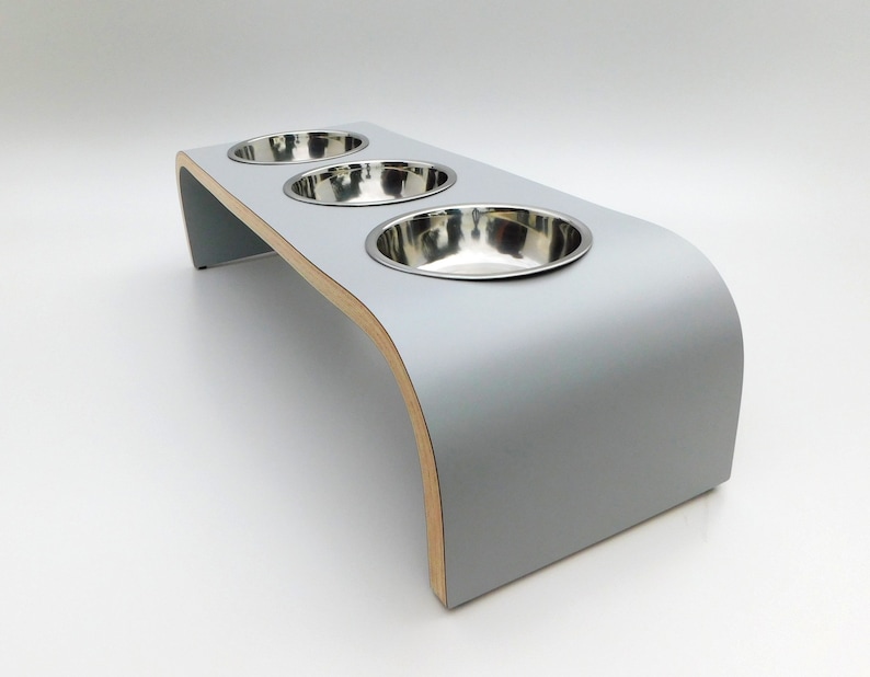 Angled view of our triple bowl raised dog feeder in a light grey finish on a white background with three stainless steel bowls and showing the natural wood edge finish.