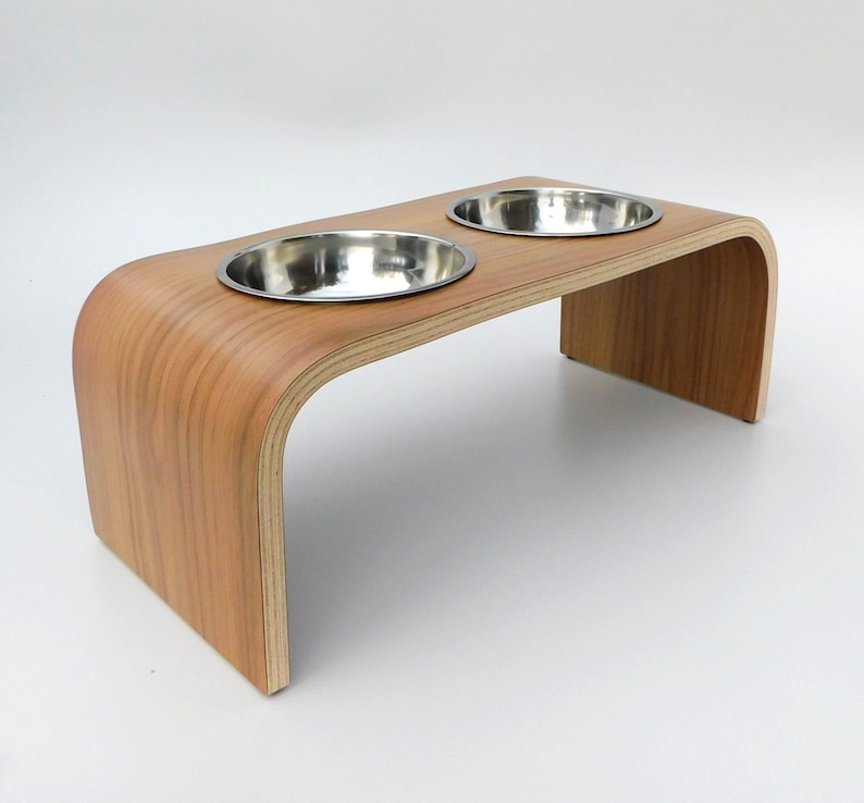 Angled view of an easy to clean non slip elevated pet feeder in a walnut finish holding 2 stainless steel bowls and a natural wood trim on a white background.