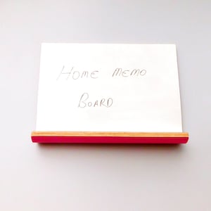 Front view of a whiteboard with pink on the reverse in landscape form with a shelf ideal for pens or keys with a natural wood trim on a wall.