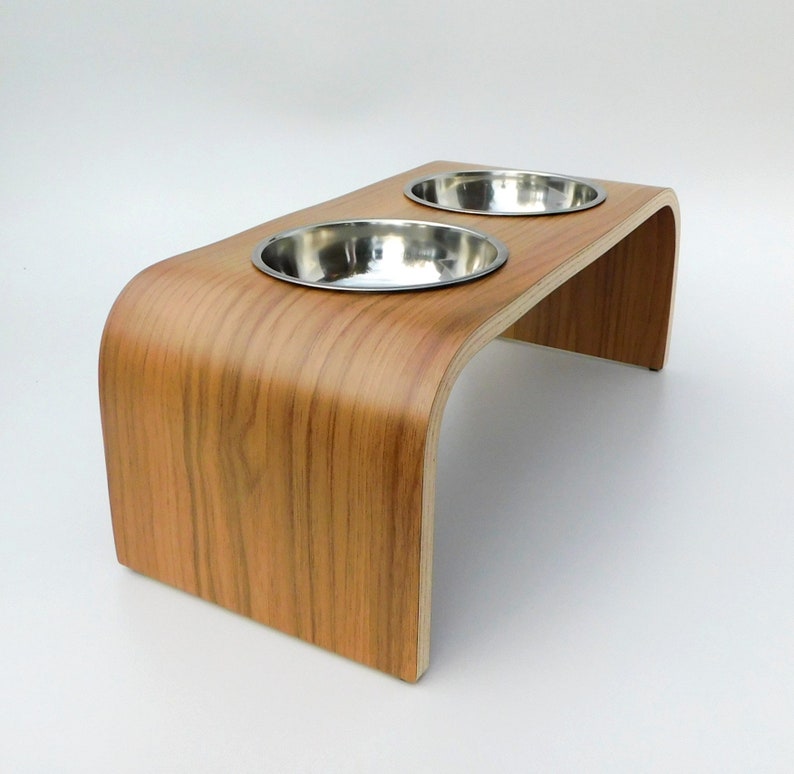 Angled view of a raised dog bowl stand in a walnut finish holding 2 stainless steel bowls and natural wood trim on a white background.