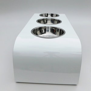 End view of our triple bowl raised dog feeder in a white gloss finish on a white background with three stainless steel bowls and showing the natural wood edge finish.
