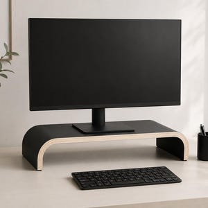 May include: A black computer monitor stand with a curved, U-shaped design and exposed light-coloured wood edges. The stand features a smooth matte black surface and supports a black computer monitor, with a black keyboard placed in front of it.